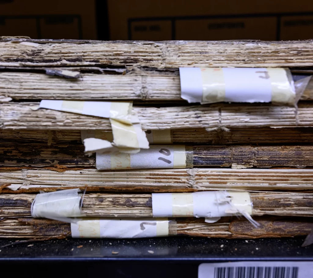 A stack of bound periodicals on a shelf showing exposed spines and old labels with tape.
