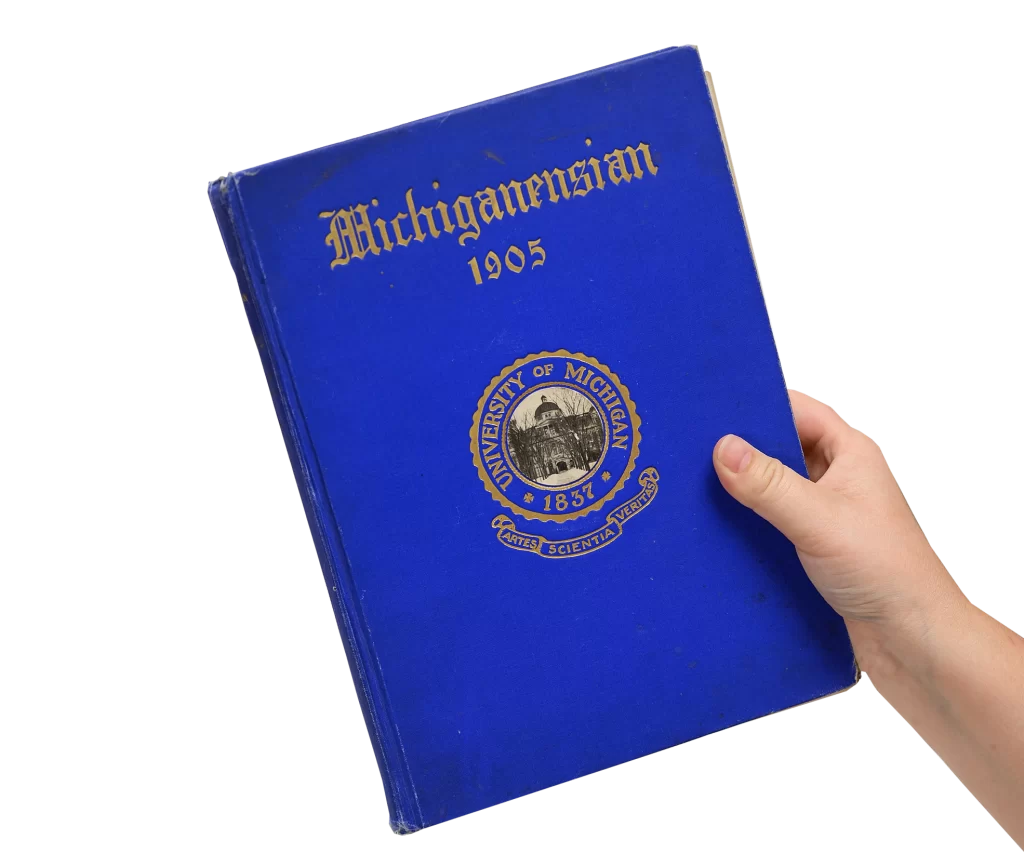 A hand holds a bright blue book that says "Michiganensian 1905" at the top in gold letters.