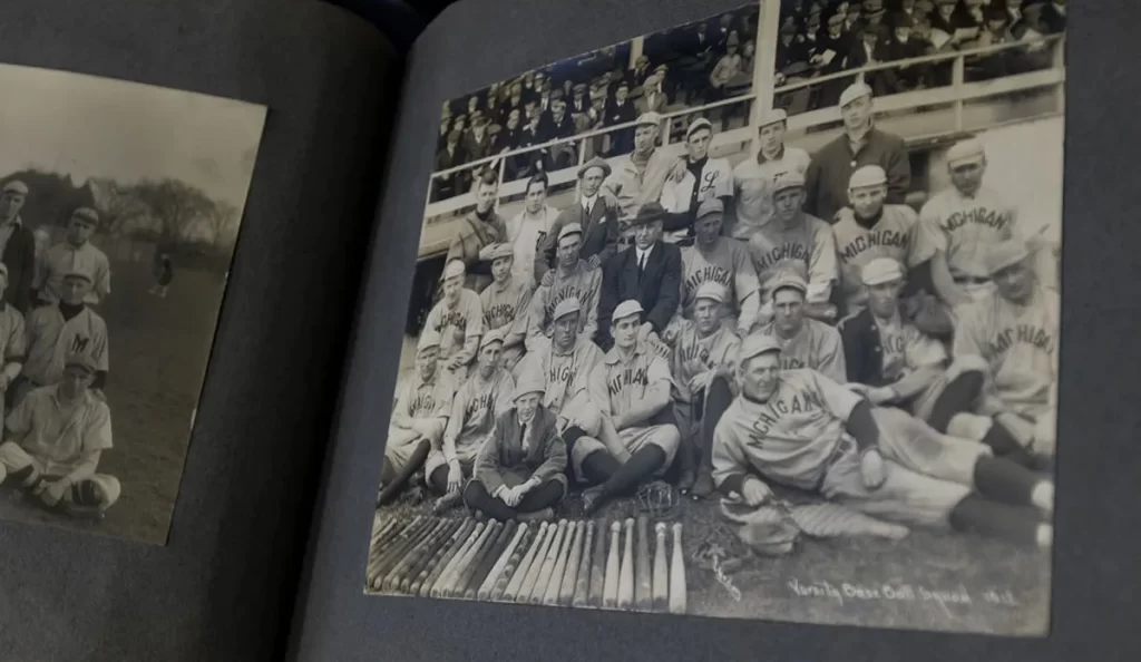 A historic scrapbook is open with old, black-and-white baseball photos on both the left and right sides of the spine.