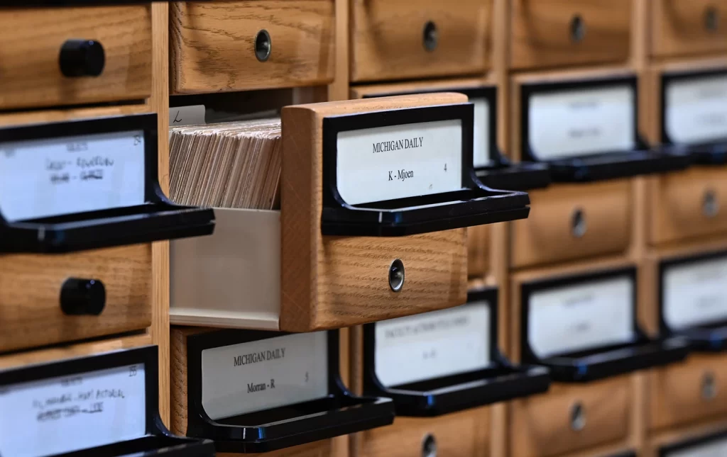 A brown card catalog drawer labeled "Michigan Daily" is partially pulled out revealing a stack of light-colored cards inside.