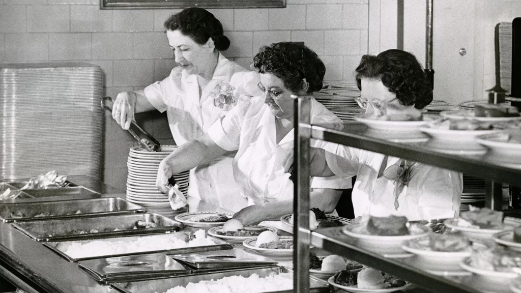 Three female cafeteria workers serving food in the West Quad dormitory cafeteria.