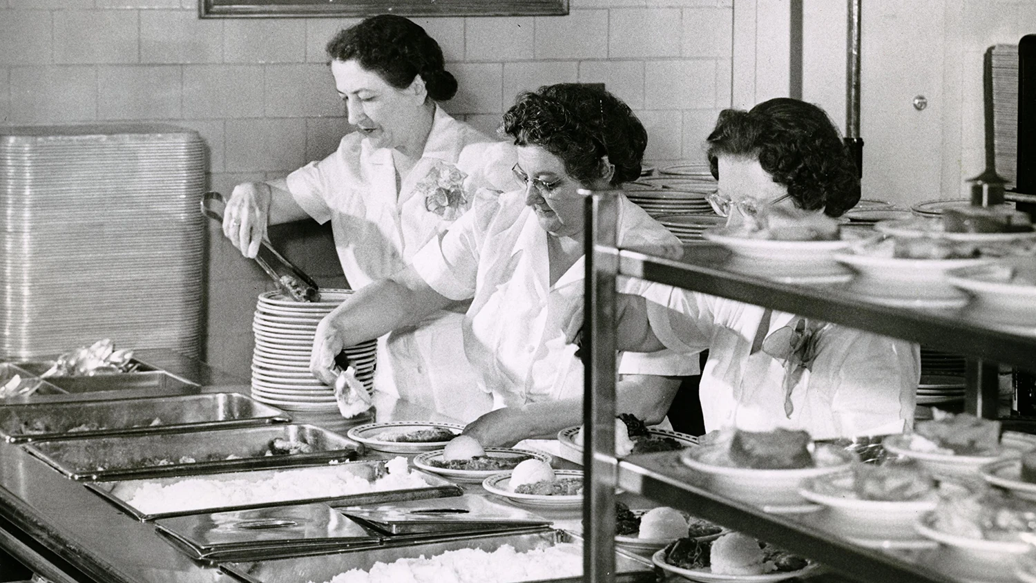 Three female cafeteria workers serving food in the West Quad dormitory cafeteria.