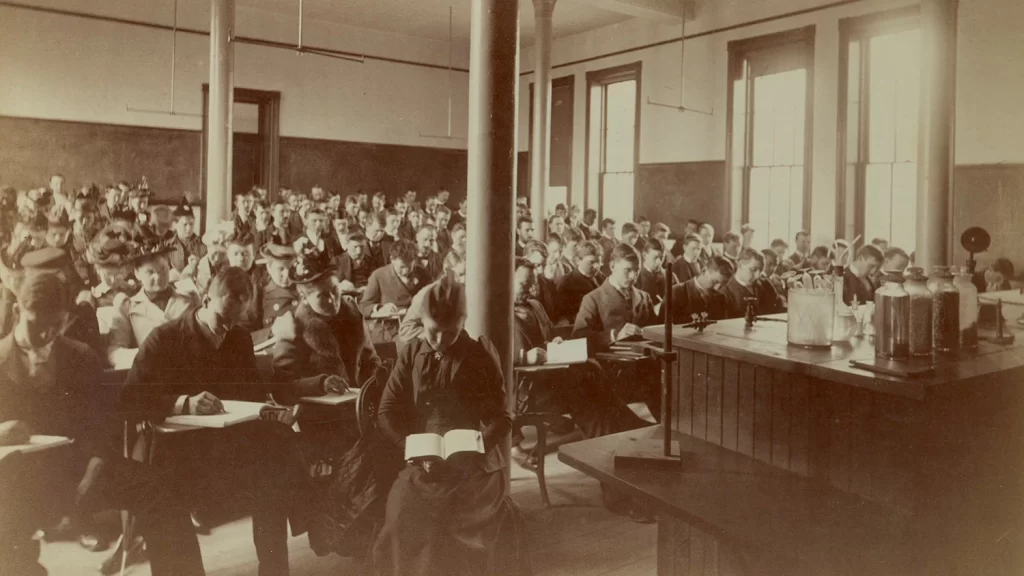 Nineteenth century male and female students reading in class.