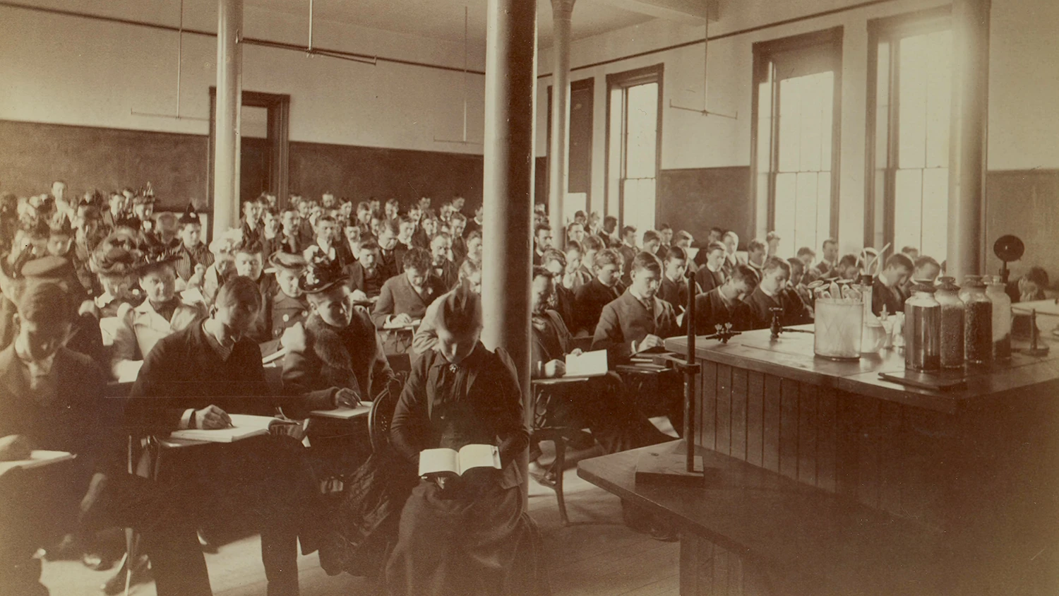 Nineteenth century male and female students reading in class.