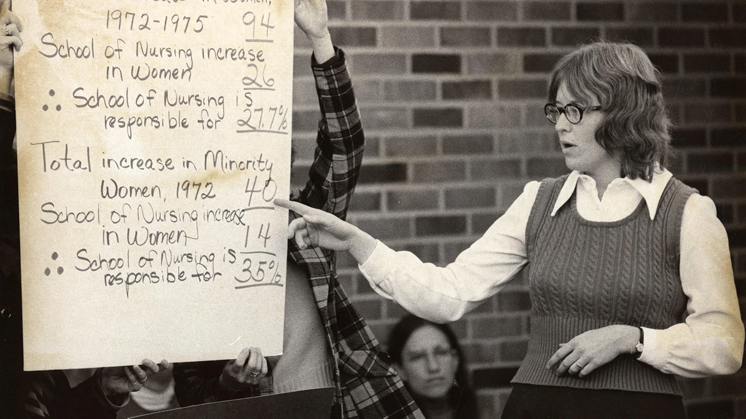 Graduate student Kathleen Shortridge pointing to a poster with numbers of female and minority student enrolled at U-M in 1974.