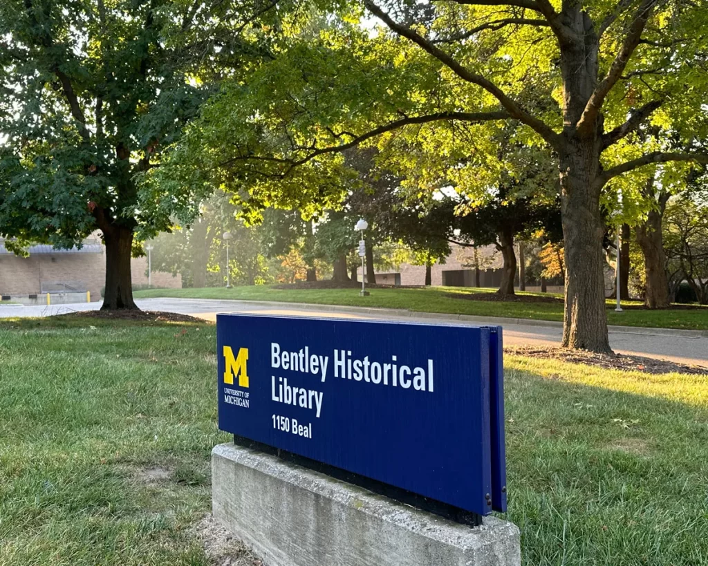 A blue sign with white text says Bentley Historical Library and is surrounded by green grass and trees.