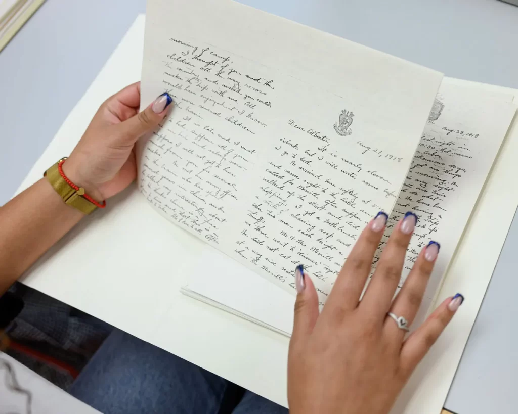 An open folder on a table with two hands holding old letters with cursive writing.