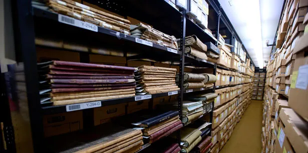 Shelves in an archive filled with old books and boxes lining both sides of an aisle.